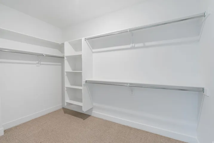 Built-in shelving, multiple hanging rods, and neutral carpet flooring