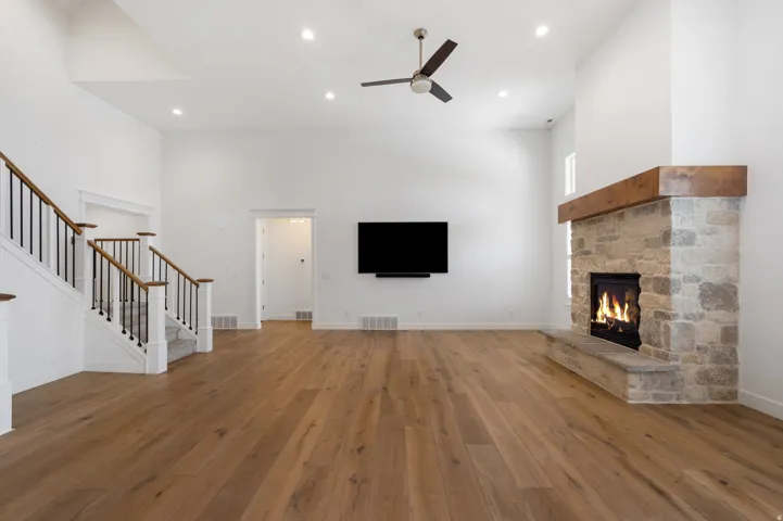 Spacious living area featuring high ceilings, wood-finish flooring, recessed lighting, and a stone fireplace with a wood mantle