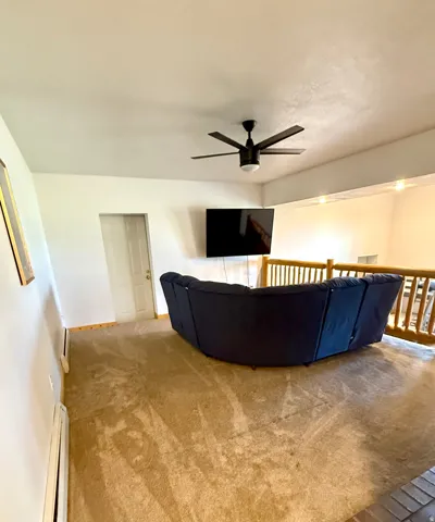 Carpeted loft area featuring a ceiling fan, wall-mounted television, and a wooden railing overlooking the space below
