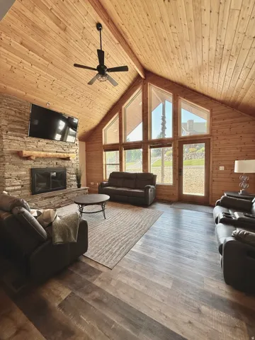 Spacious living area featuring a vaulted wood-paneled ceiling, stone-clad fireplace with a wood mantel, and large windows