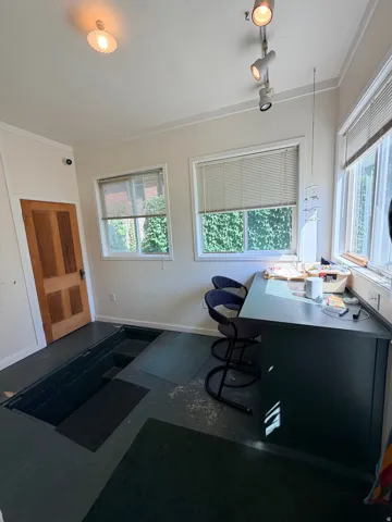 Bright home office featuring expansive windows with cellular blinds, recessed ceiling lighting, wood-finish entry door, and dark composite flooring throughout