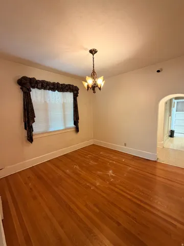 Hardwood flooring, arched doorway, window with blinds, and ceiling-mounted light fixture