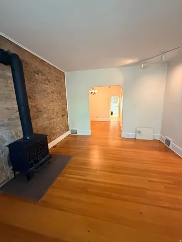 Hardwood flooring, exposed brick accent wall, black wood-burning stove, tile hearth, archway