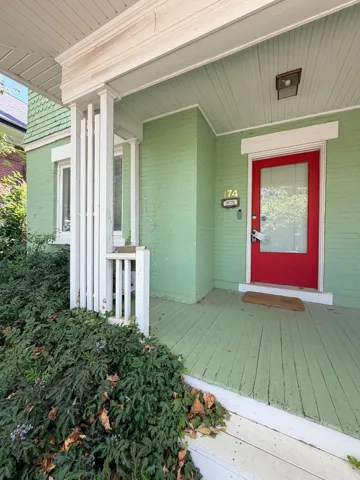 Covered front porch featuring a red entry door with glass panel, wood-finish flooring, and white porch columns