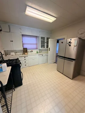 Kitchen featuring white cabinetry, a built-in window, a stainless steel refrigerator, and patterned vinyl flooring