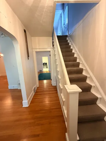 Welcoming entry hallway featuring warm wood-finish flooring, crisp white walls, and a custom white railing