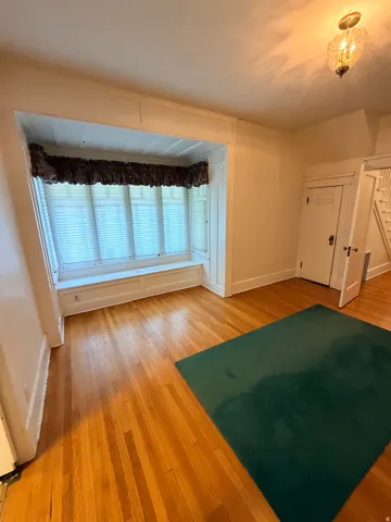 Hardwood flooring, bay window with built-in bench seating, classic interior door, decorative ceiling light fixture, and staircase with wood newel post