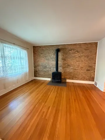 Exposed brick accent wall, wood-burning stove, wood flooring, and window with natural light