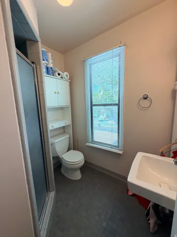 Tiled flooring, built-in shelving, window with blinds, wall-mounted sink, and a glass-enclosed shower