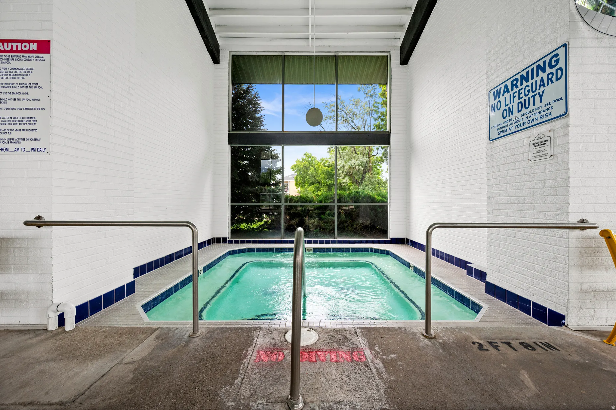 Indoor spa with surrounding white brick walls, blue tile accents, and stainless steel grab rails