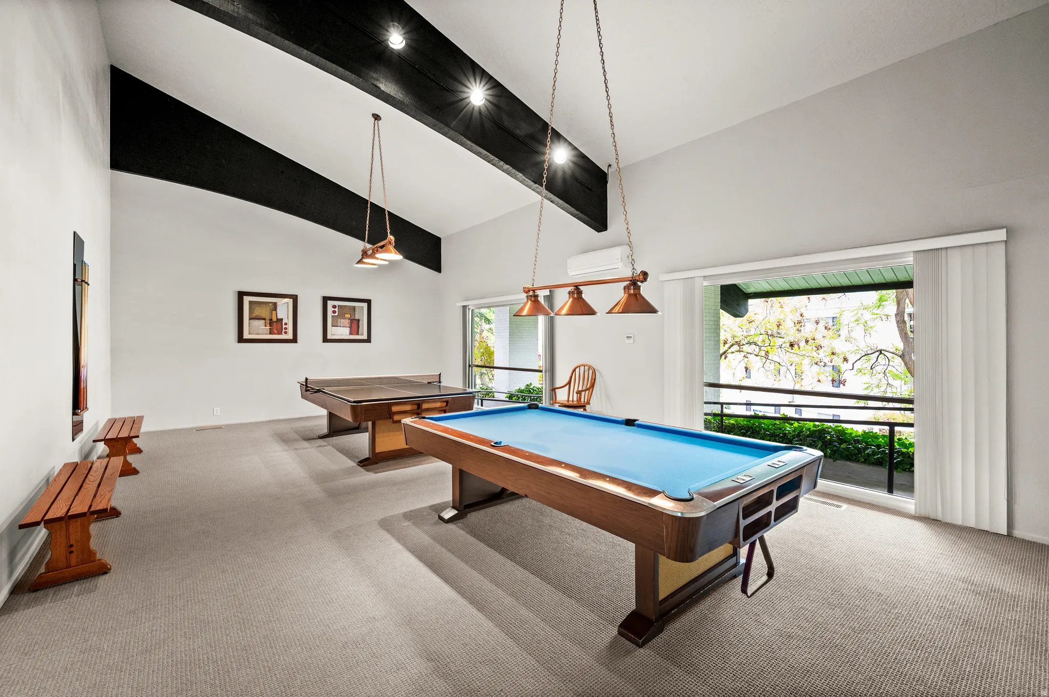 Vaulted ceilings with exposed beams, carpeted flooring, and abundant natural light from expansive windows