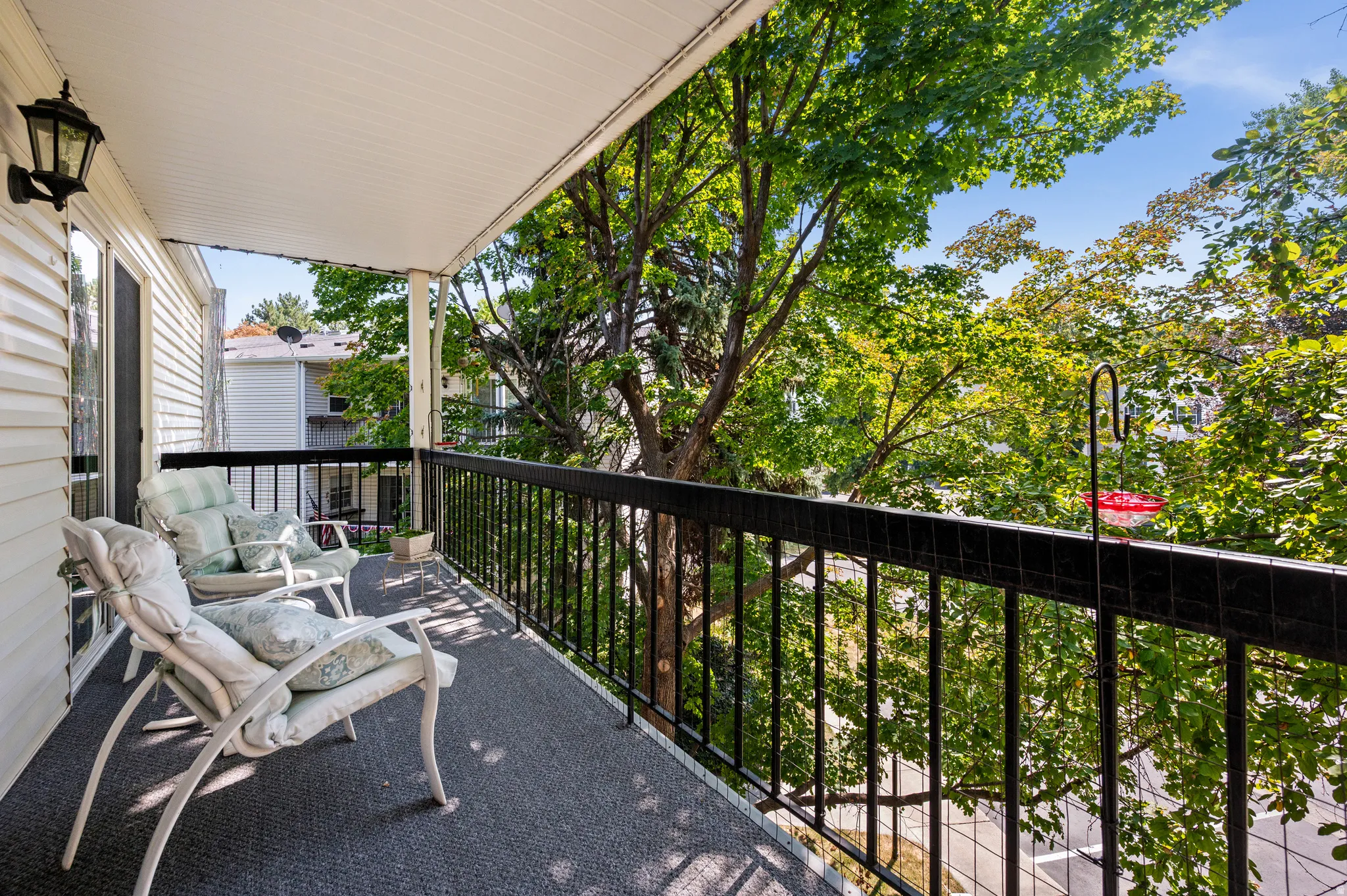 Covered balcony with black metal railings, textured dark gray flooring, and a wall-mounted exterior light fixture