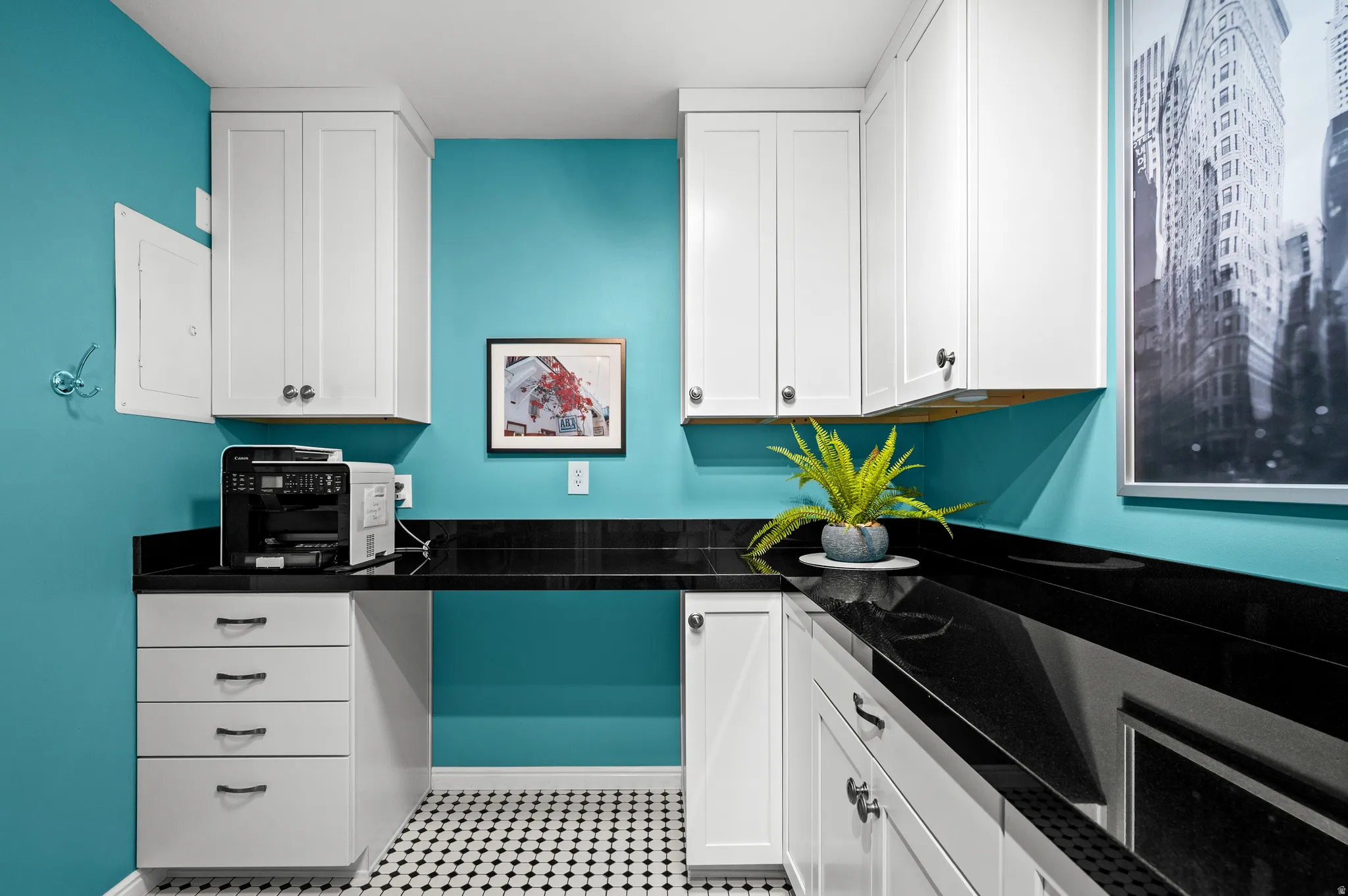 White shaker-style cabinetry, black countertop, checkerboard tile flooring, and a built-in desk area