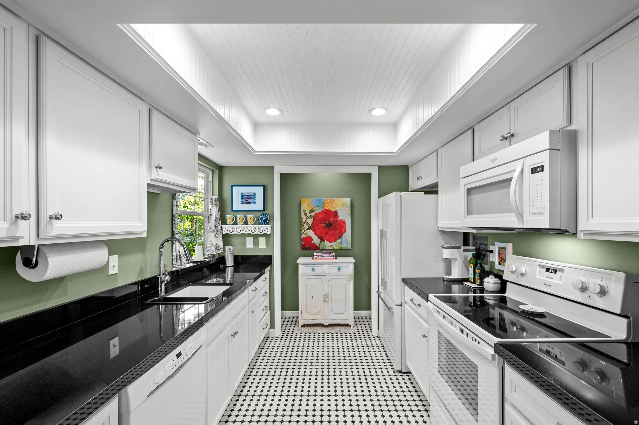 Galley kitchen with white cabinetry, black countertops, stainless steel sink, and a black and white tiled floor