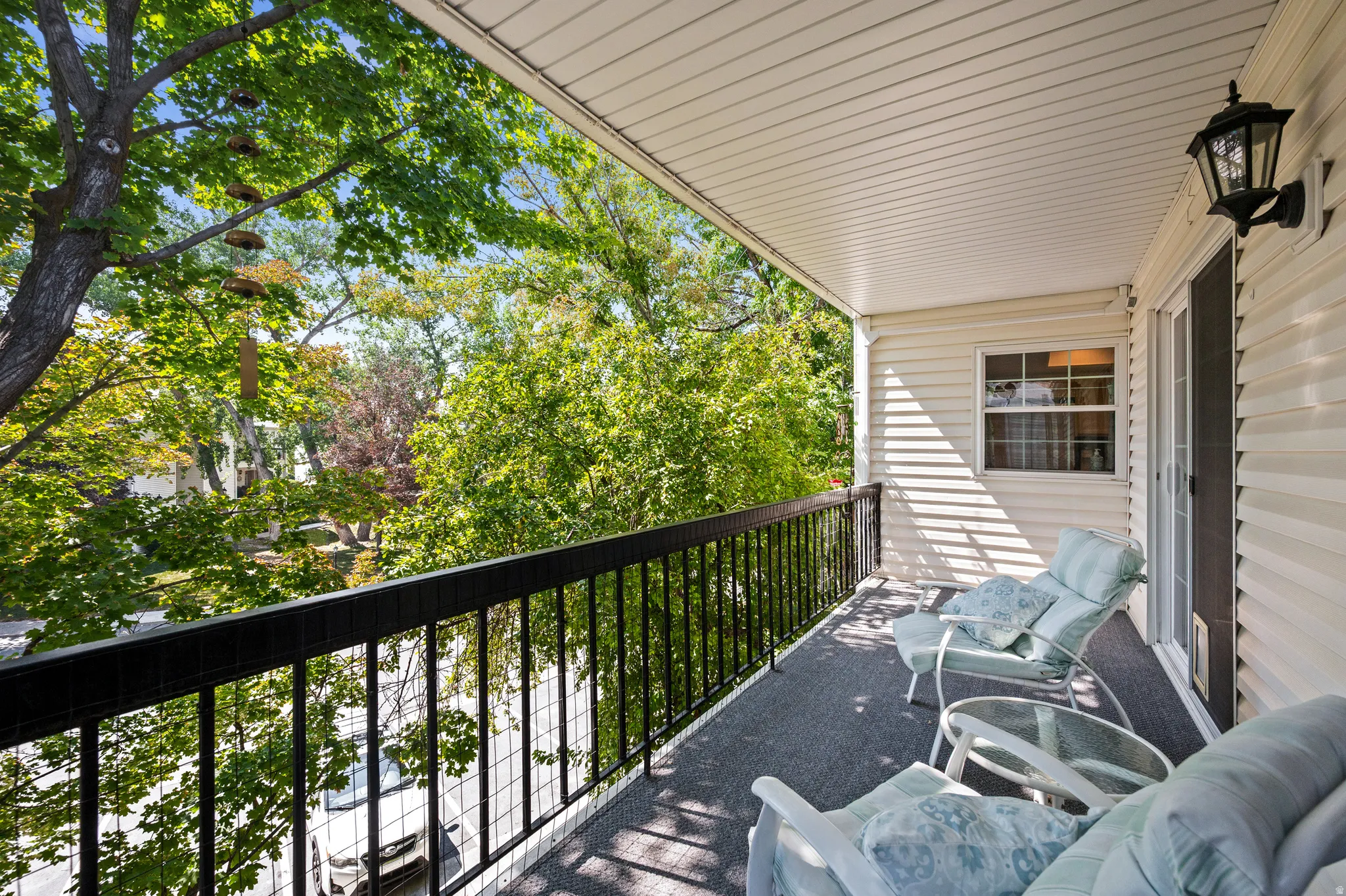 Covered balcony featuring a privacy wall, metal railing, outdoor wall sconce, sliding glass door, and a textured floor