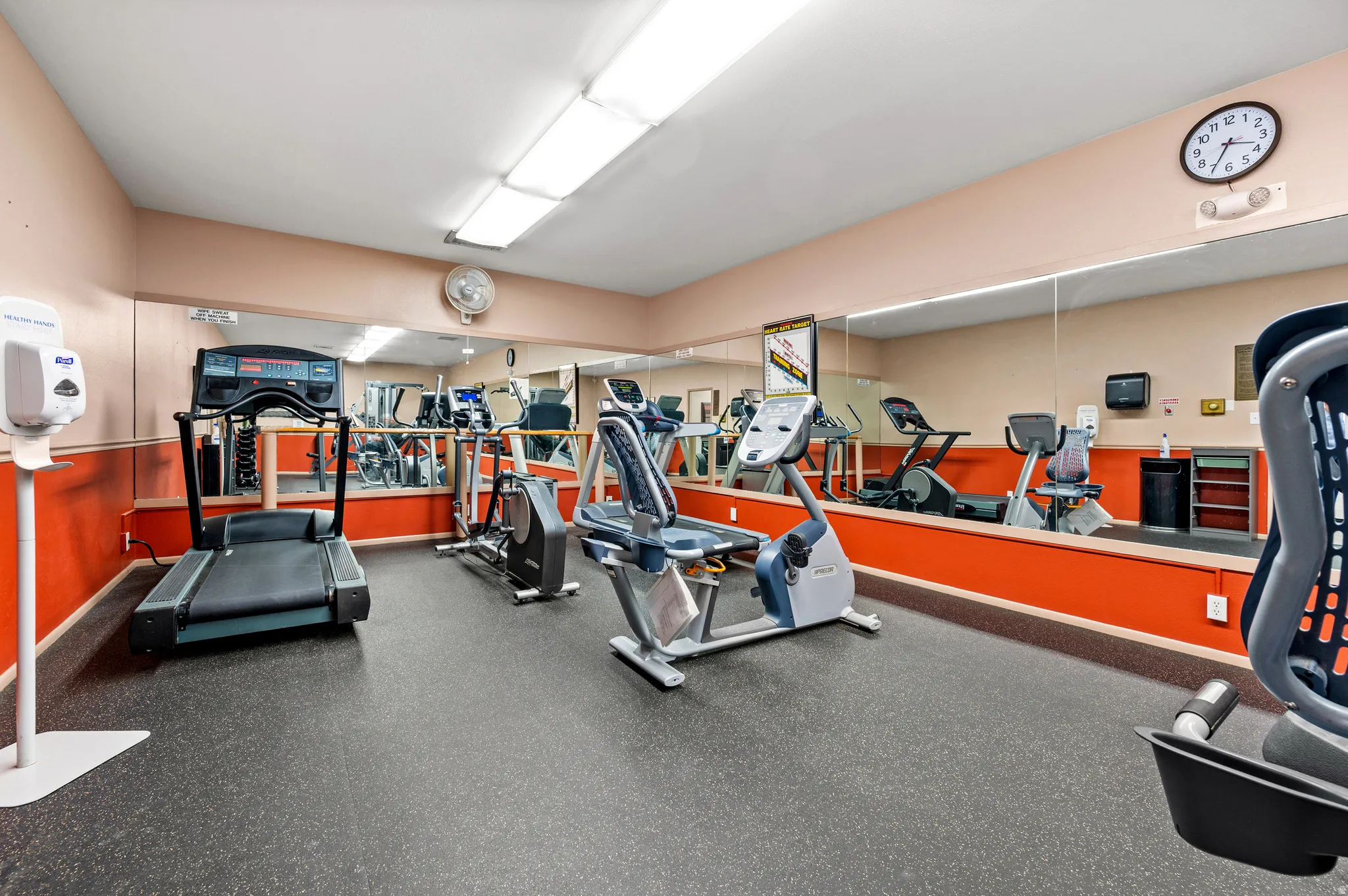 Fitness center featuring a rubberized floor, mirrored wall, recessed lighting, and wall-mounted clock