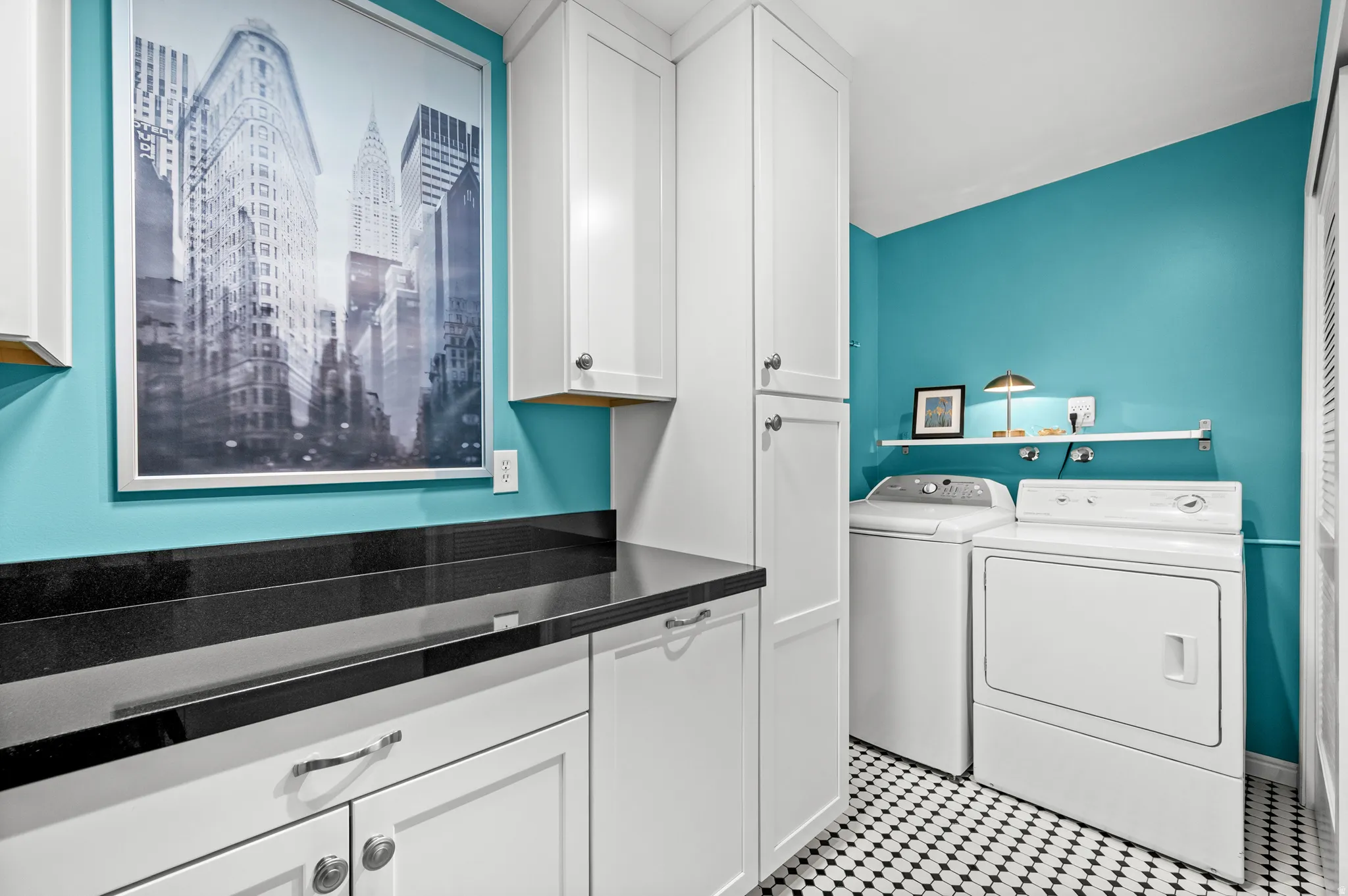 White shaker cabinetry with dark hardware, black countertop, white and black mosaic tile flooring, and a built-in shelf