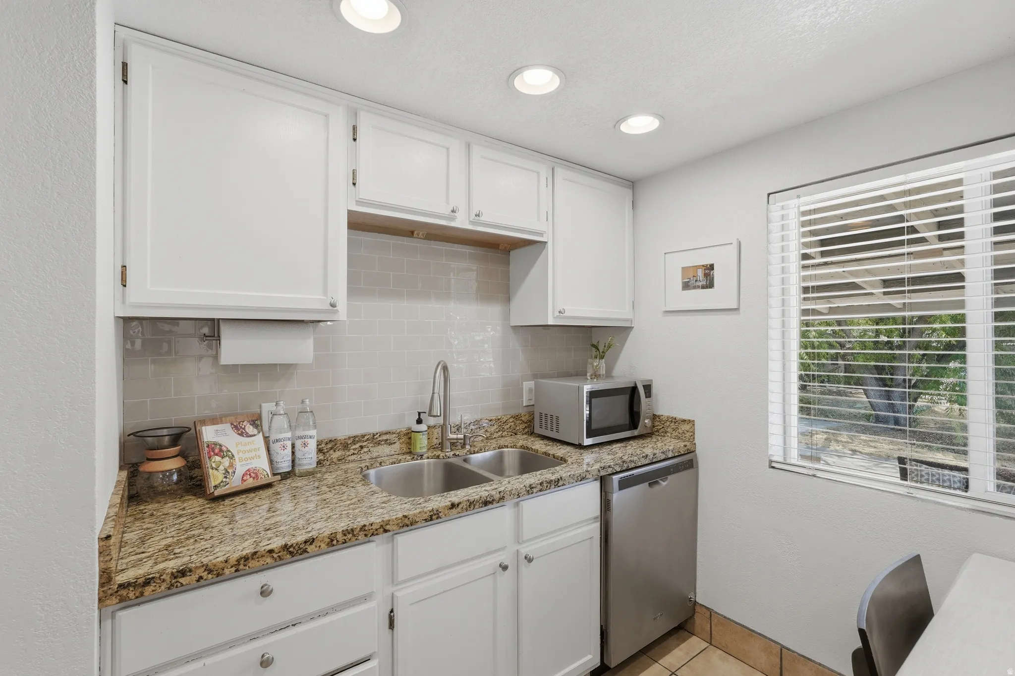 White cabinetry with brushed nickel hardware, granite-style countertops, subway tile backsplash, stainless steel double basin sink, and recessed ceiling lighting
