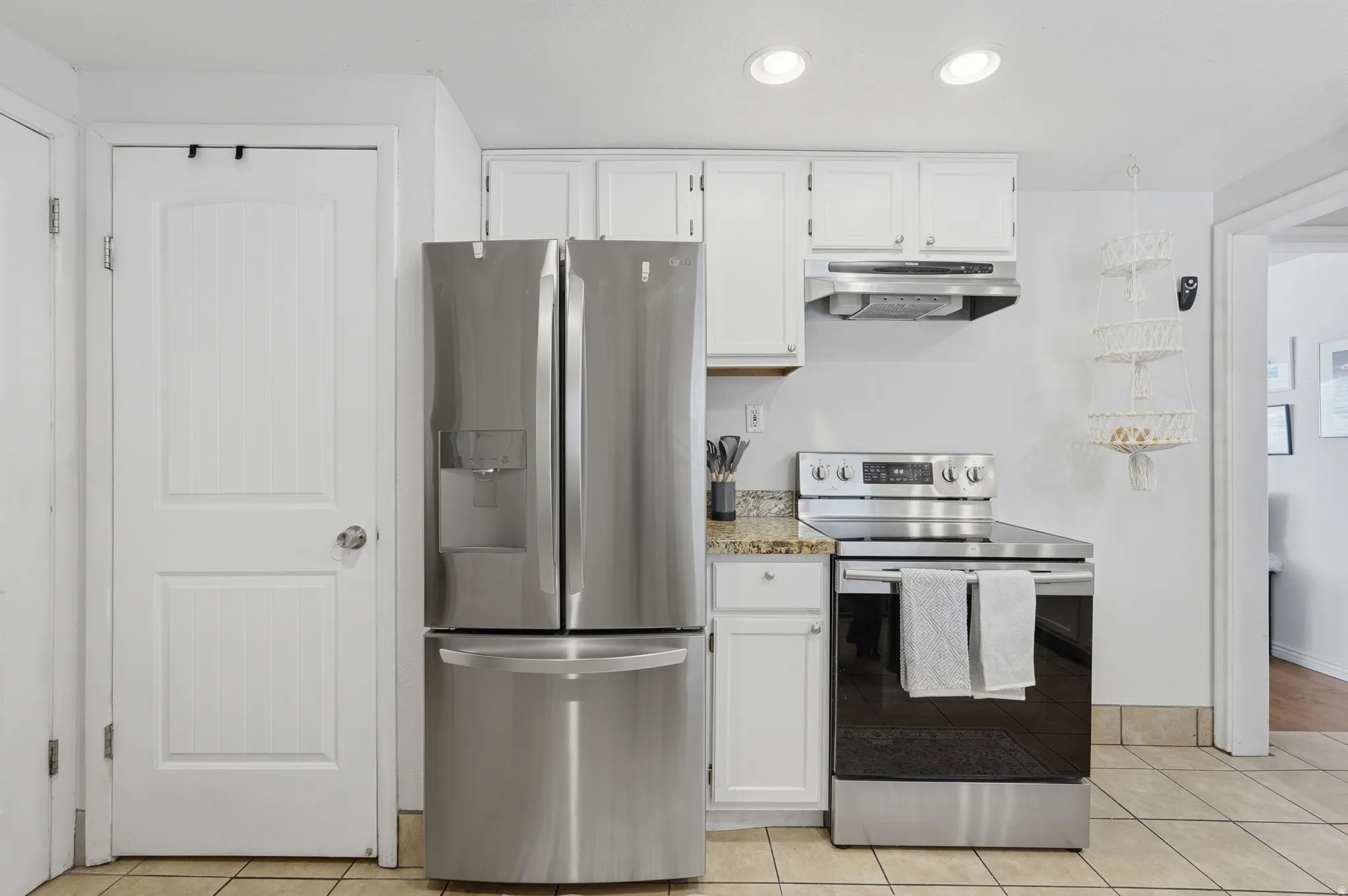 Updated kitchen featuring stainless steel French-door refrigerator, electric range with convection oven, tile countertops, white cabinetry with hardware accents, and recessed ceiling lighting