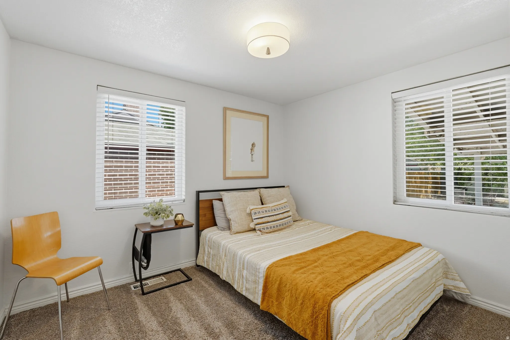 Bright secondary bedroom featuring dual windows with plantation shutters, wood-finish flooring, neutral wall finishes, and a ceiling-mounted light fixture