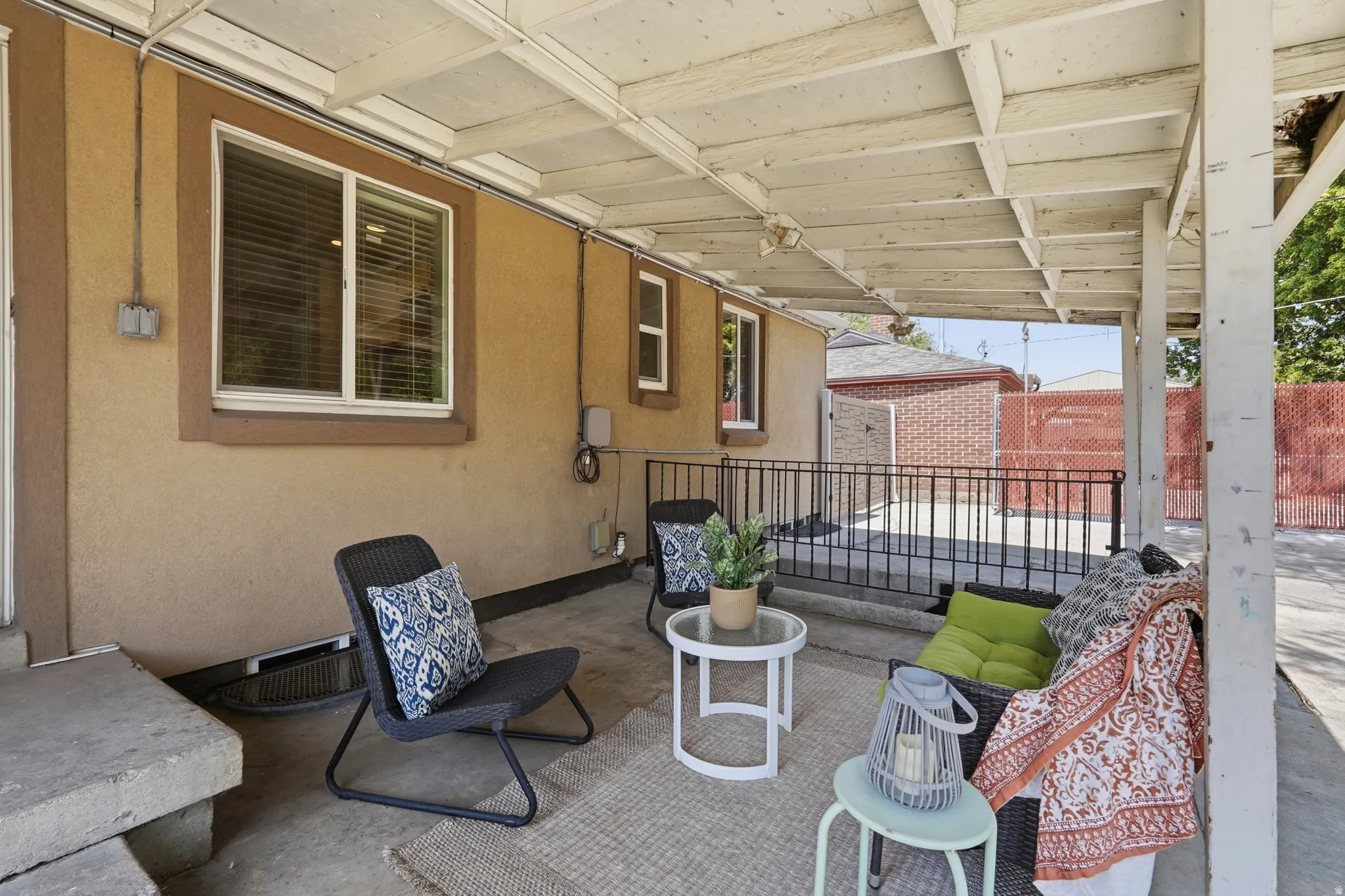 Covered patio with white beam ceiling and support columns, featuring built-in seating along the perimeter railing, concrete flooring, and access to multiple windows of the adjoining residence