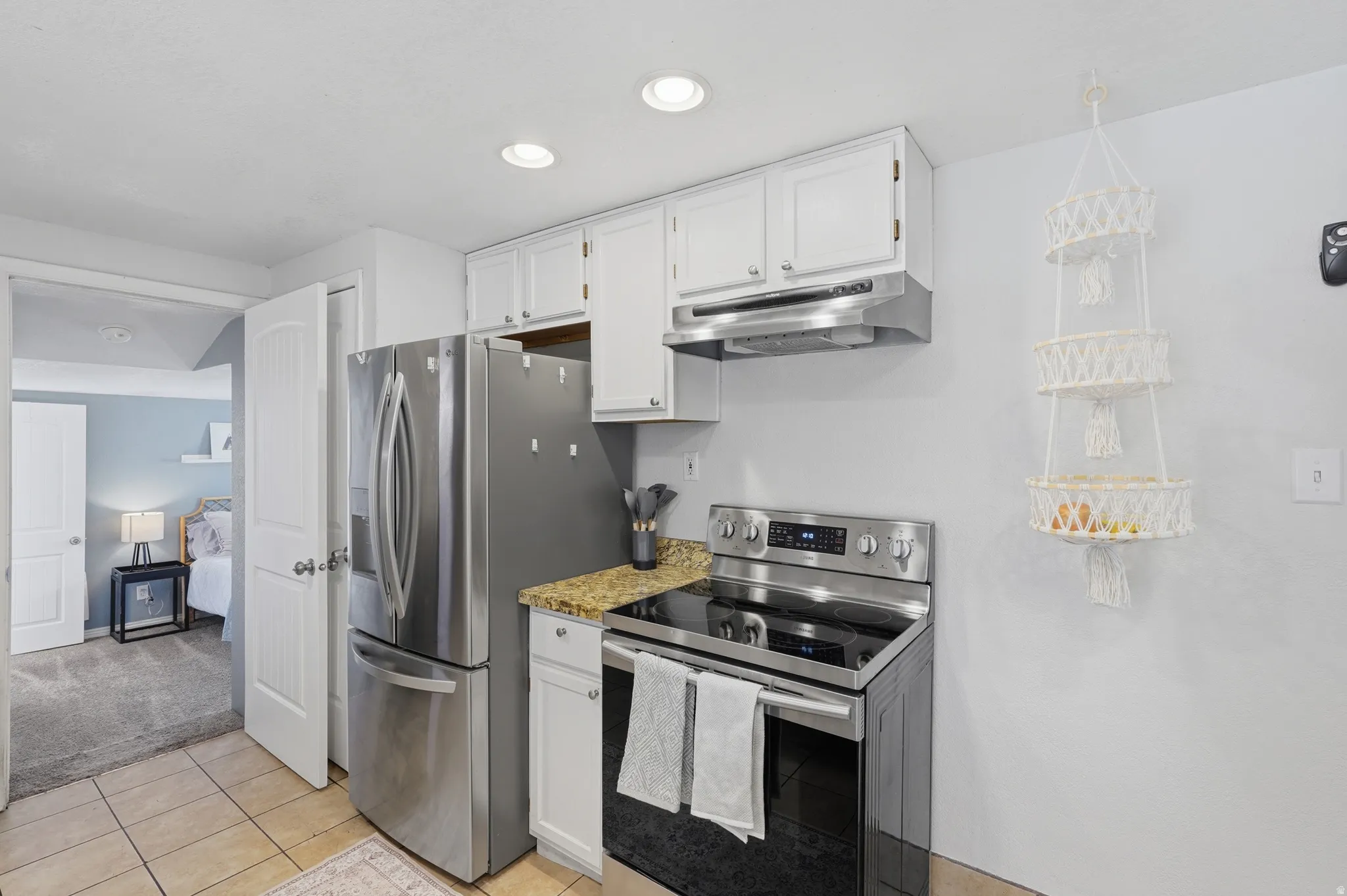 Kitchen featuring stainless steel appliances, white cabinetry, granite-style countertops, tile flooring, and recessed lighting