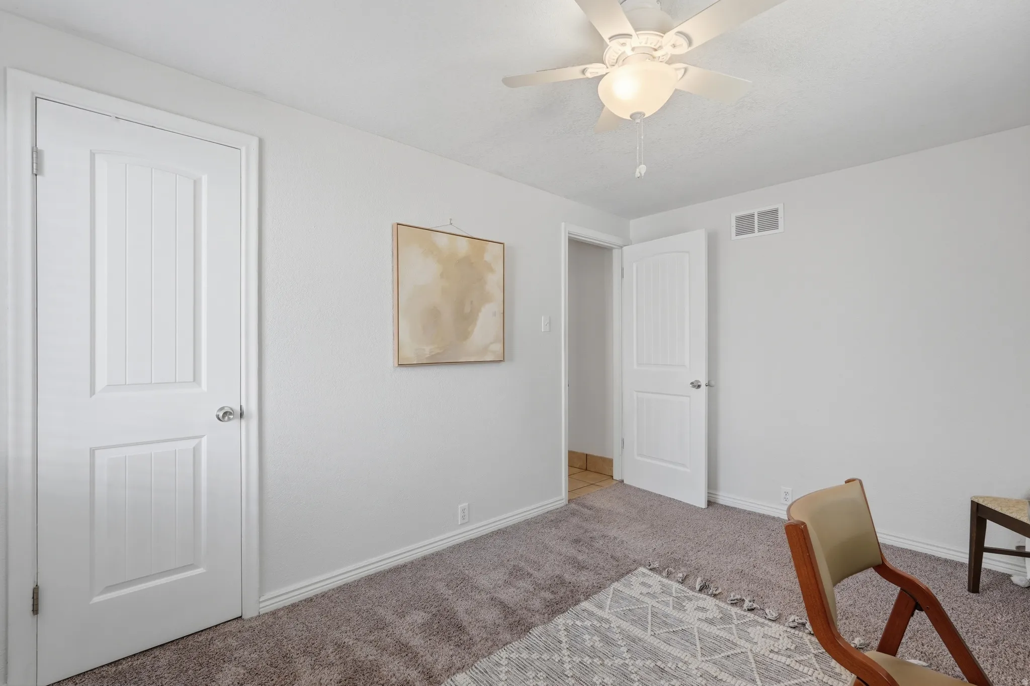 Bright secondary bedroom featuring neutral carpet flooring, white six-panel doors, ceiling fan with integrated lighting, and a framed accent wall piece
