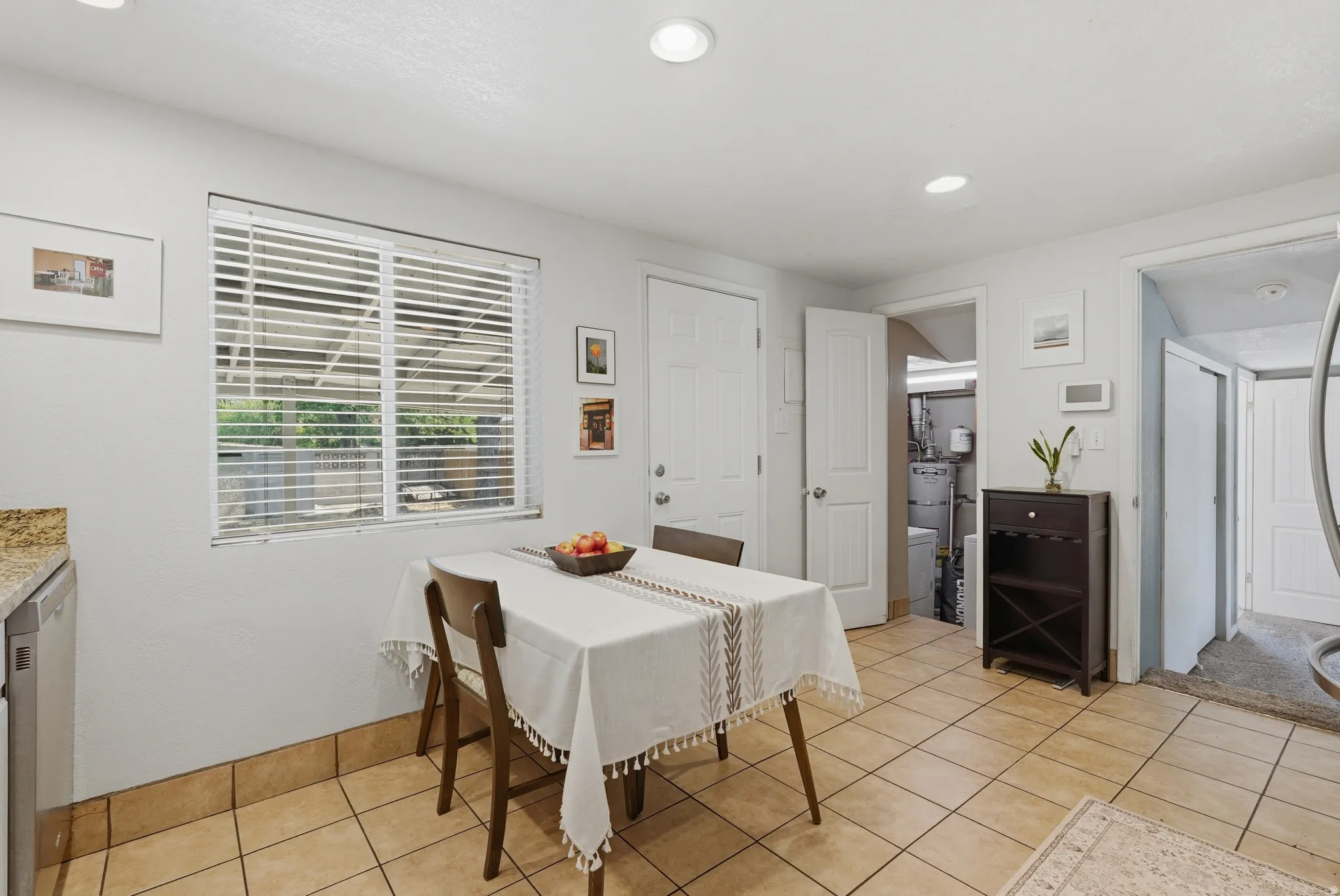 Bright dining area featuring tile flooring, shuttered windows with natural light, and a dark wood dresser with decorative mirror