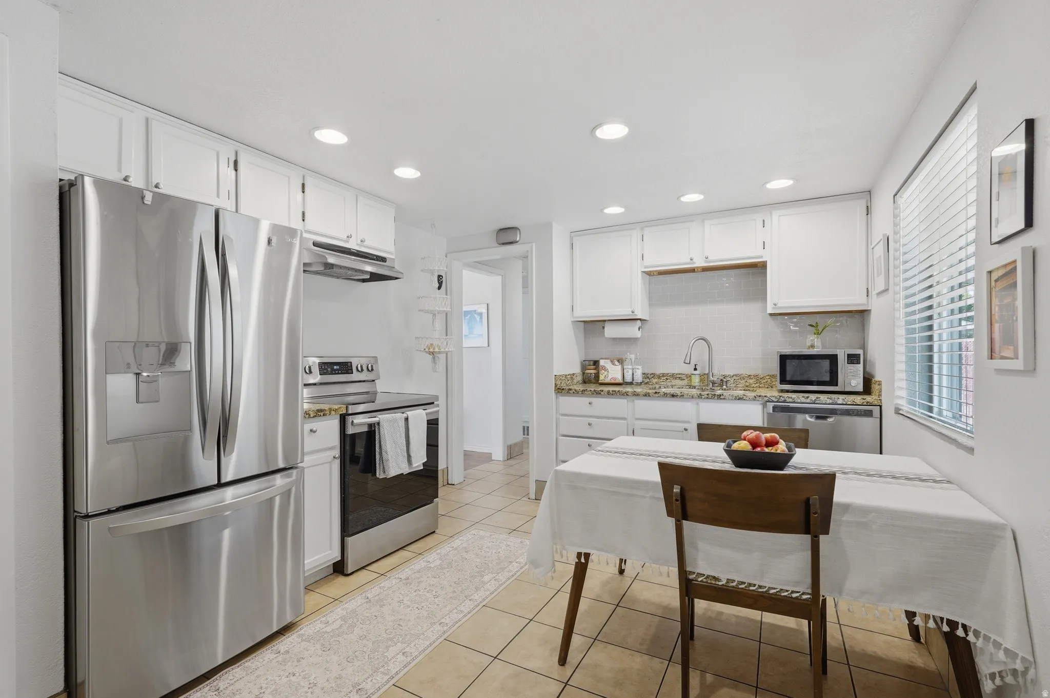 Kitchen featuring white cabinetry, stainless steel appliances, granite-style countertops, tile backsplash, and recessed lighting