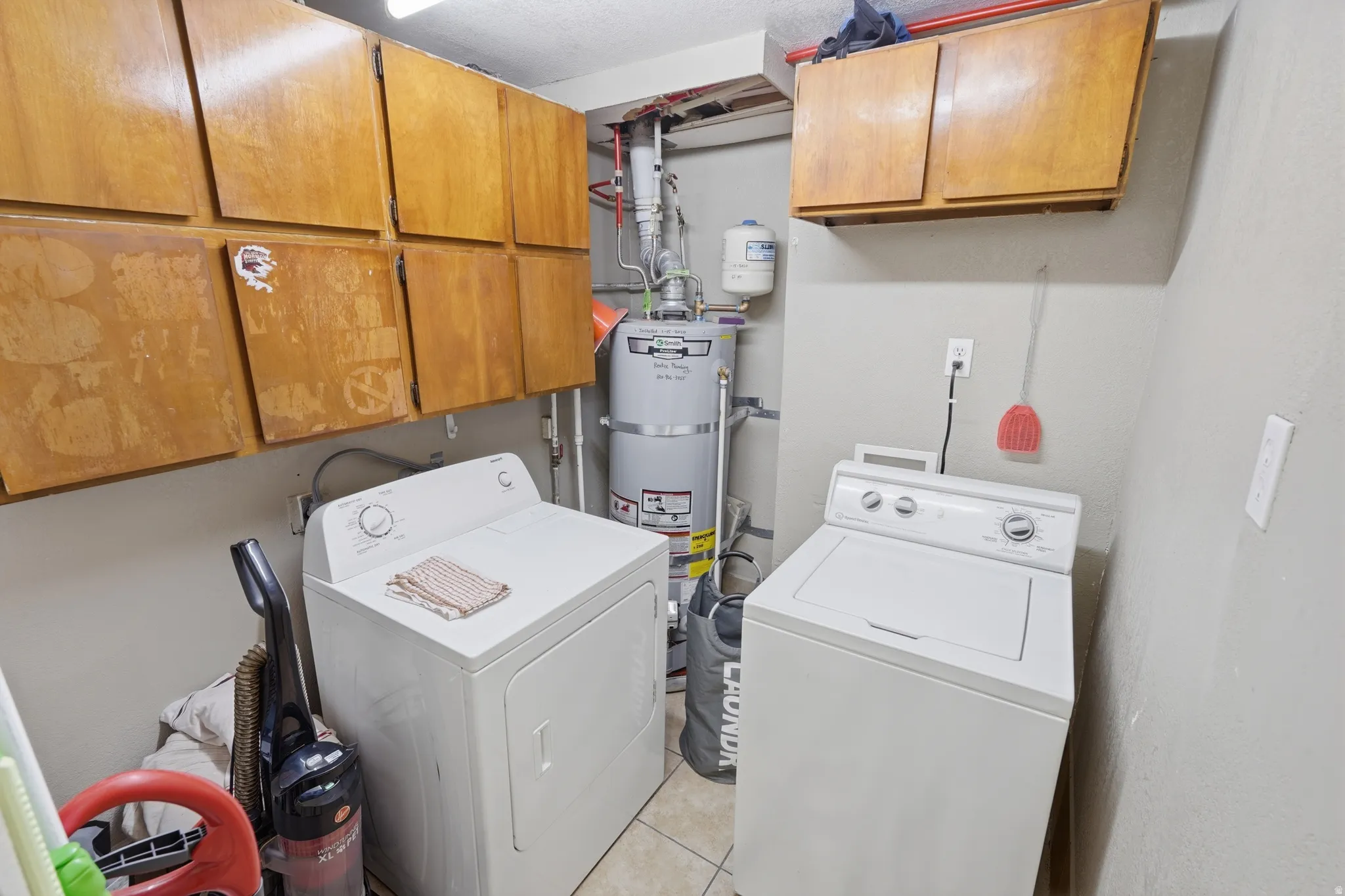 Laundry room featuring side-by-side washer and dryer units, ample cabinetry storage with wood-finish finishes, water heater, and tile flooring