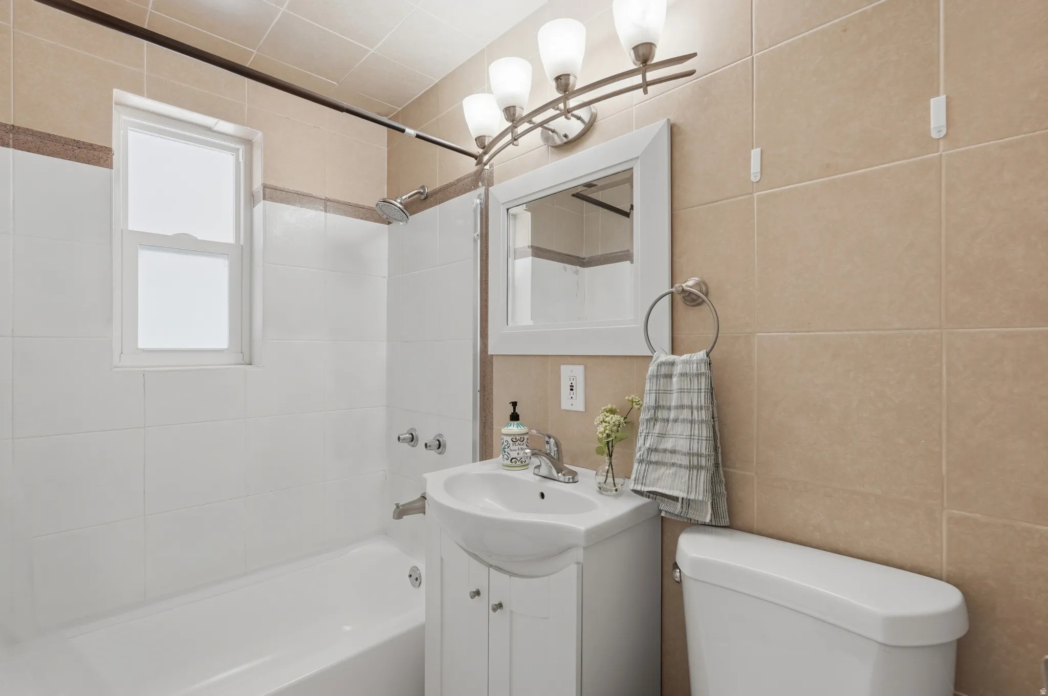 Bright bathroom featuring a ceramic pedestal sink with chrome faucet, white cabinetry with storage, frameless mirror with integrated lighting, and a white subway tile surround