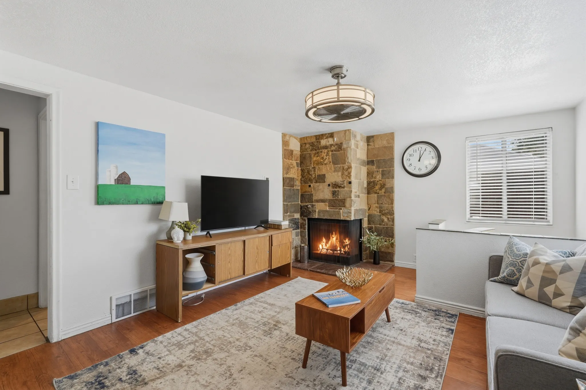 Living area featuring a stone-clad fireplace, wood-finish flooring, and a ceiling-mounted light fixture