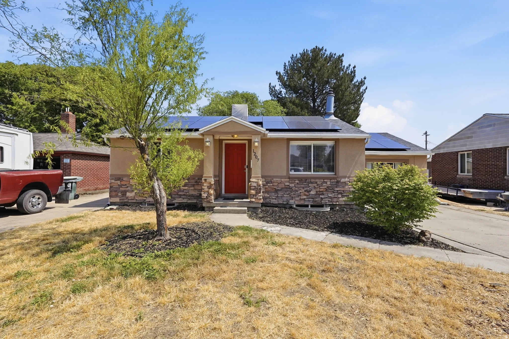 Charming single-story residence featuring a tan stucco exterior with stone accents, red entry door, and large front-facing window