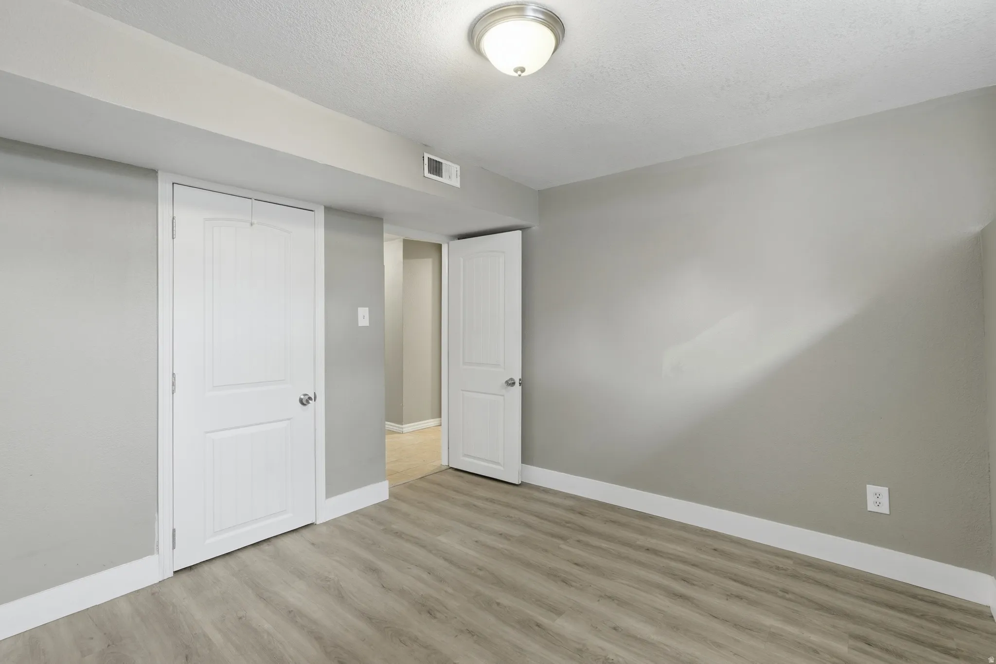 Bright bedroom showcasing wood-finish flooring, neutral walls, and abundant natural light