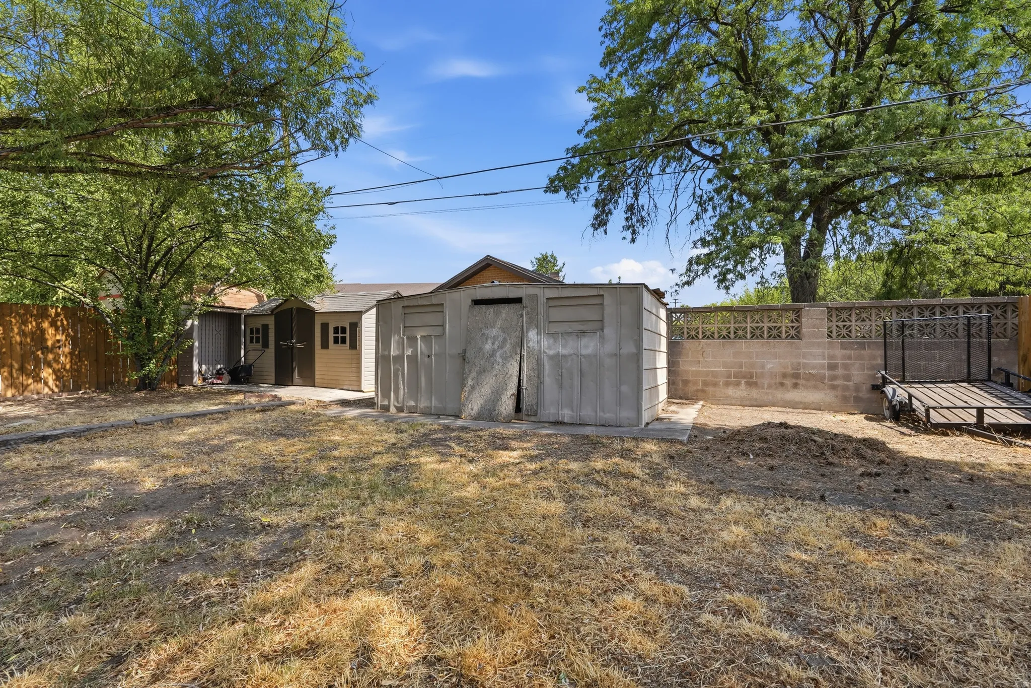 Detached storage shed, concrete block wall, wood fence, and mature trees