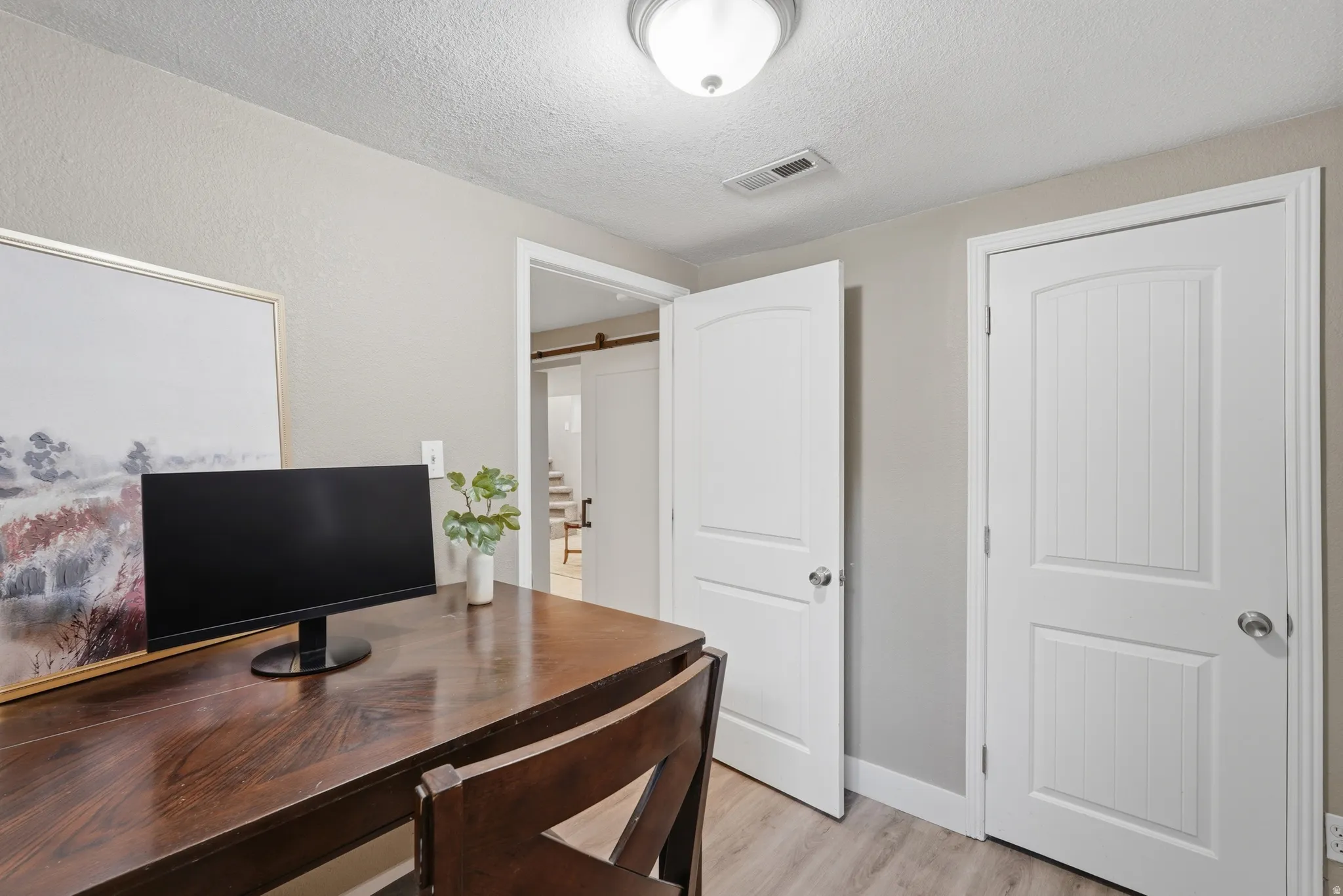 Light wood-finish flooring, white paneled doors, and a flush mount ceiling light