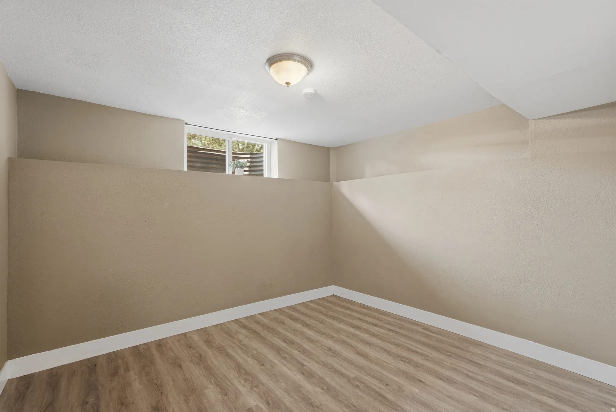 Recessed window with horizontal blinds, overhead ceiling light fixture, wood-finish flooring, and light-toned walls