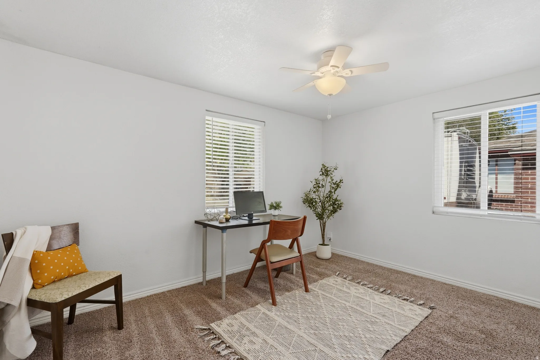 Plush carpeted room featuring a ceiling fan with integrated lighting, two windows with blinds, and white painted walls