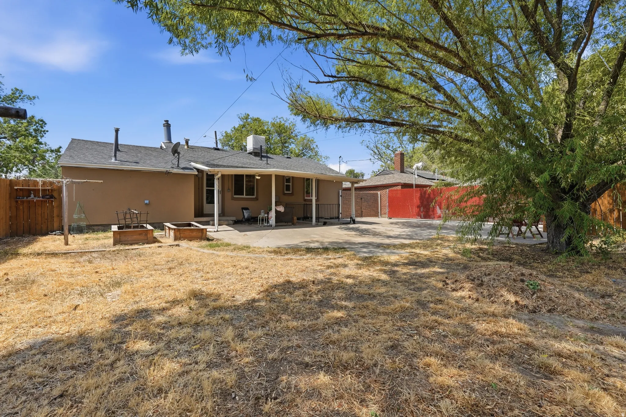 Spacious single-story residence with a covered patio, detached red outbuilding, and expansive grounds anchored by mature shade trees