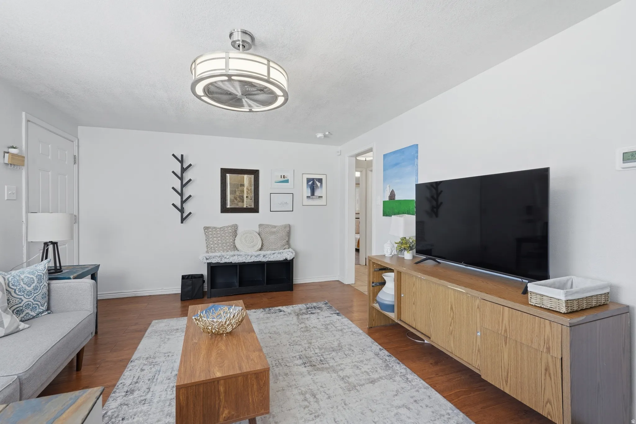 Bright living room showcasing hardwood flooring, a wood-finish media console with ample storage, and a modern ceiling fan with integrated lighting
