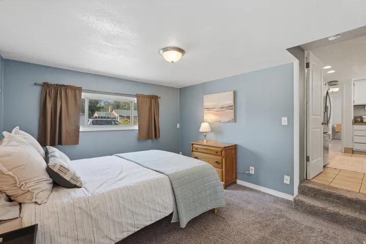 Serene primary bedroom showcasing soft blue walls, carpeted flooring, and abundant natural light from a large window with brown drapery