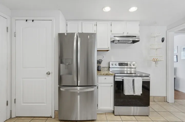 Updated kitchen featuring stainless steel French-door refrigerator, electric range with convection oven, tile countertops, white cabinetry with hardware accents, and recessed ceiling lighting