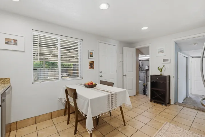 Bright dining area featuring tile flooring, shuttered windows with natural light, and a dark wood dresser with decorative mirror
