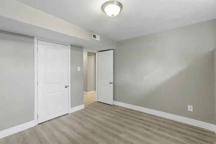 Bright bedroom showcasing wood-finish flooring, neutral walls, and abundant natural light