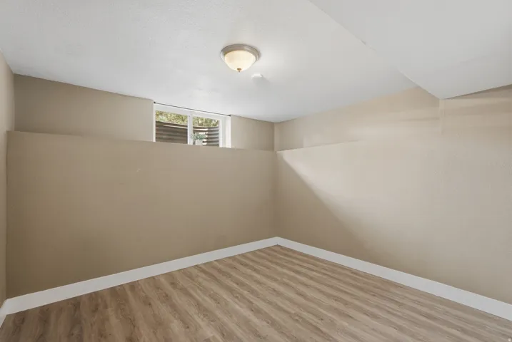 Recessed window with horizontal blinds, overhead ceiling light fixture, wood-finish flooring, and light-toned walls