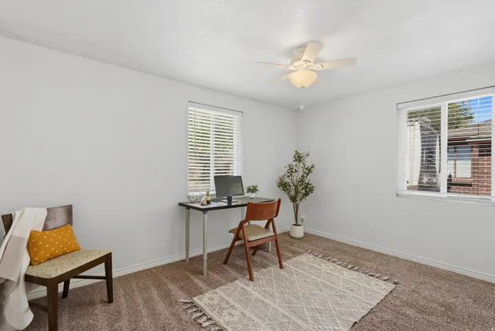 Plush carpeted room featuring a ceiling fan with integrated lighting, two windows with blinds, and white painted walls