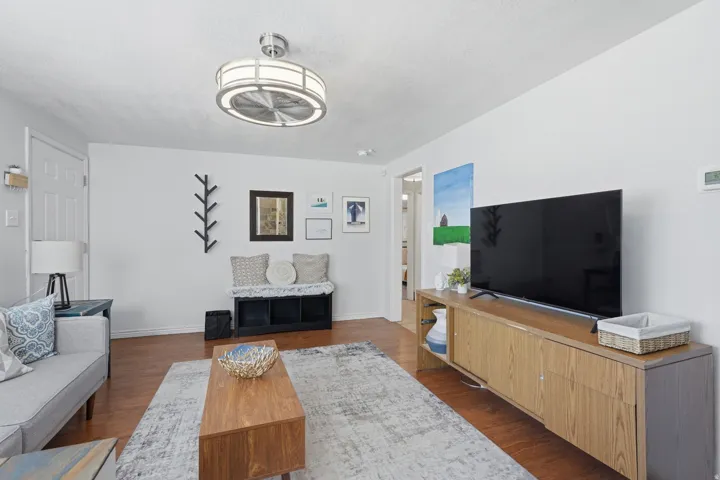 Bright living room showcasing hardwood flooring, a wood-finish media console with ample storage, and a modern ceiling fan with integrated lighting