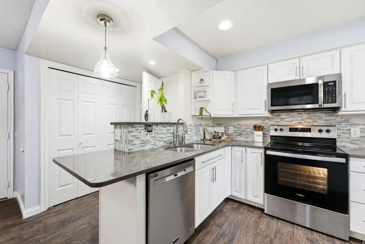 Renovated kitchen featuring crisp white cabinetry, stainless steel appliances including a double wall oven and microwave, subway tile backsplash, and a curved island with dark quartz countertops and seating