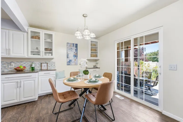 Bright kitchen and dining area featuring white cabinetry with glass-front upper cabinets, subway tile backsplash, wood-finish flooring, and a round dining table positioned near French doors that open to an outdoor patio