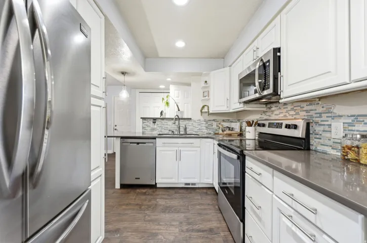 Kitchen featuring white cabinetry, stainless steel appliances, dark countertops, and a mosaic tile backsplash